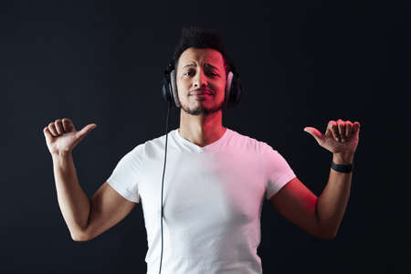 Smile Young African American man portrait wearing headphones and enjoy music over black Background. Red light reflection on face.の写真素材