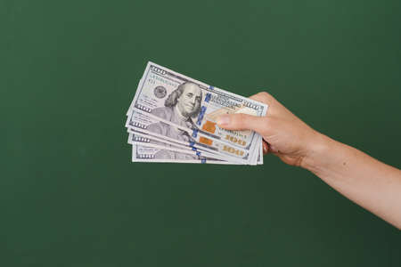 Woman hand with stack of dollars isolated on green background with copy space