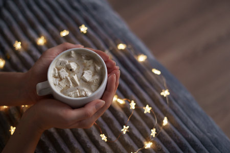 Female hands hold a cup of coffee with marshmallow on gray background with glowing lights. Flat lay,...