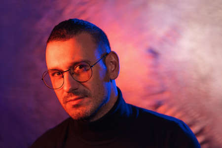 Neon portrait of serious man wearing glasses with black frame and dark turtleneck sweater on cosmic silver multicolored backgroundの写真素材
