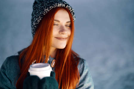 Girl drinking hot coffee while walking in the evening. Feeling happy in big city. Spending winter vacationsの写真素材