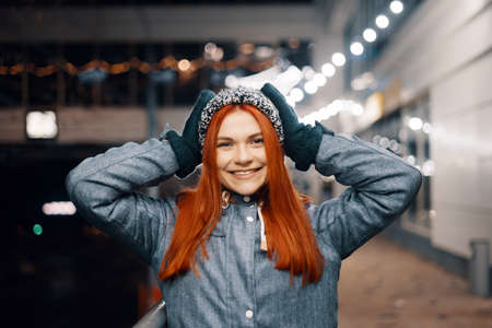 Outdoor night photo of young beautiful happy smiling girl enjoying festive decoration, in street of european city, wearing knitted beanie hatの写真素材