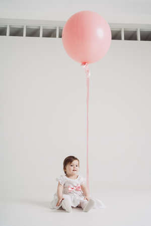 A little girl with a big pink balloon in white dress on a white backgroundの写真素材