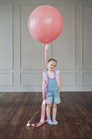 A girl with a big pink balloon playing indoors. Cheerful kid holding a balloonの写真素材