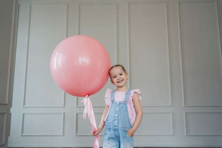 A girl with a big pink balloon playing indoors. Cheerful kid holding a balloonの写真素材
