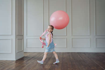 A girl with a big pink balloon playing indoors. Cheerful kid holding a balloonの写真素材