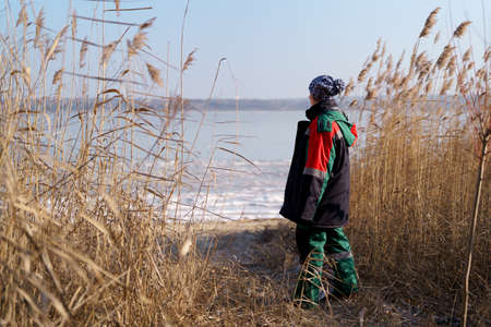 Woman in colorful winter clothes watching a frozen lake among high golden fern, beauty of nature