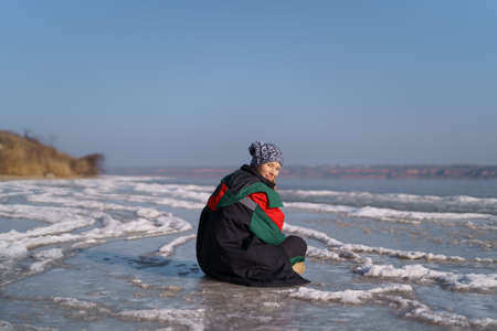 A woman in a colorful thermal costume enjoying winter while sitting and watching a frozen lake with...