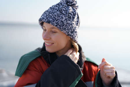 Authentic woman winter portrait aranging her wool hat smiling. She wears a warm colorful jacket