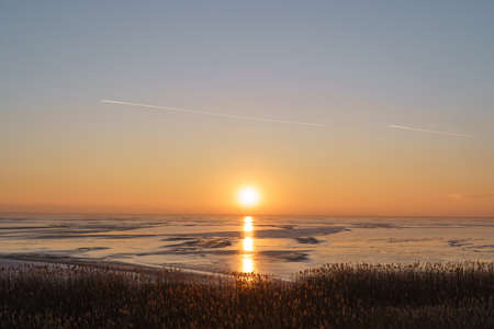 Scenic view of an orange sunset with sun reflecting in the ice of the lake. Motivational, inspirational viewの写真素材