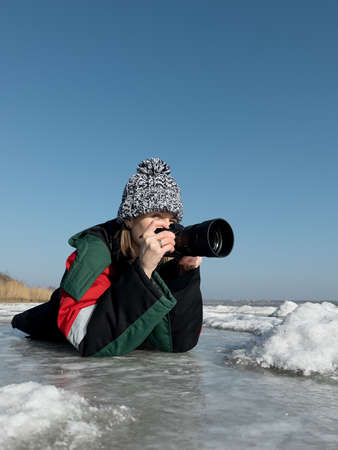 Authentic woman photographer taking pictures of natural frozen lake with a clear blue sky in...