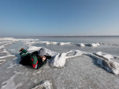 Authentic woman photographer taking pictures of natural frozen lake with a clear blue sky in background. Explorerの写真素材