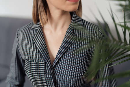 Cropped image of a woman with beautiful v neck line in a shirt with lines behind a plant