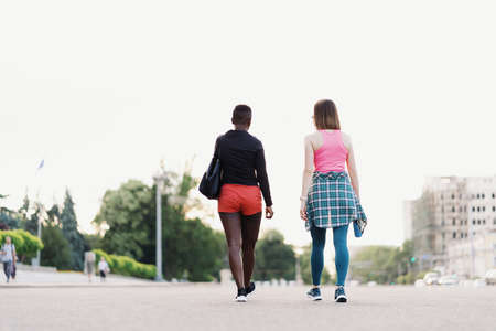 Friends back view in sportswear walking after a sport session in the city discussing . Multiethnic women having a fitness workout jogging.の写真素材
