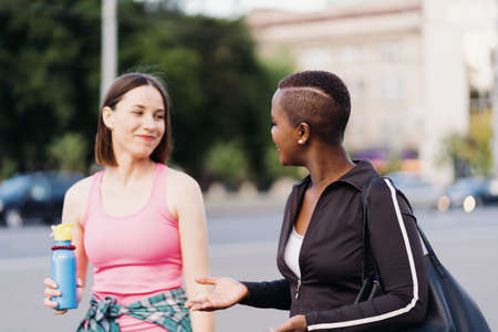 Cheerful smiling friends in sportswear walking after a sport session in the city discussing and having fun. Multiethnic women having a fitness workout jogging.の写真素材