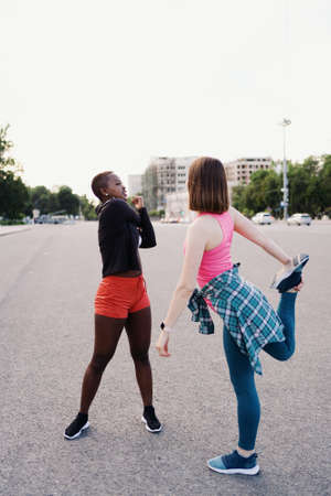 Two fit diverse young woman working out together in city square doing stretching exercise and hand extensionsの写真素材