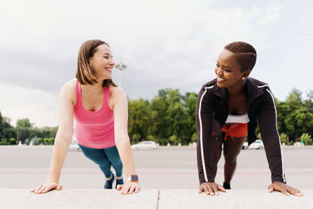 Two smiling diverse young woman in Athletic Workout Clothes are Doing a Plank Exercise working out...