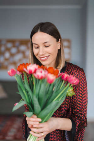 Happy woman enjoy bouquet of tulips. Housewife enjoying a bunch of flowers and interior of kitchen. Sweet home. Allergy freeの写真素材