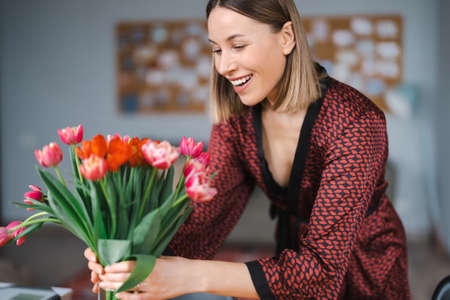 Beautiful woman arranging flowers presented by her husbant at home, happy and joyfulの写真素材