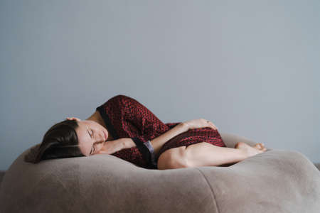 Calm serene beautiful young lady, lying down in a dream, relaxing sleep on a soft beige bean bag,...