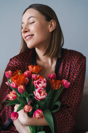 Happy woman enjoy bouquet of tulips. Housewife enjoying a bunch of flowers and interior of kitchen....