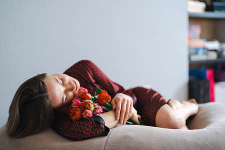 Happy woman enjoy bouquet of tulips. Housewife enjoying a bunch of flowers while relaxing on a comfy bean bag. Sweet home. Allergy freeの写真素材