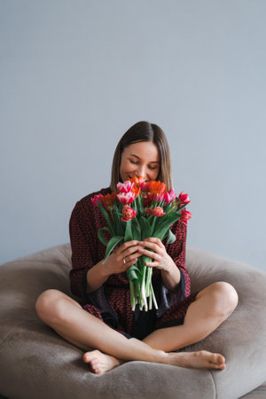 Happy woman enjoy bouquet of tulips. Housewife enjoying a bunch of flowers while relaxing on a comfy bean bag. Sweet home. Allergy freeの写真素材