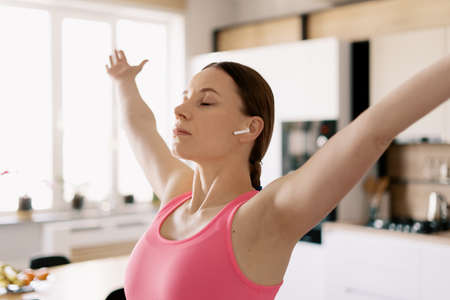 Woman closed eyes practicing yoga at home using wireless headphones