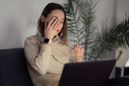 Portrait of a woman holding glasses ant touches her face being tired by working at the laptopの写真素材