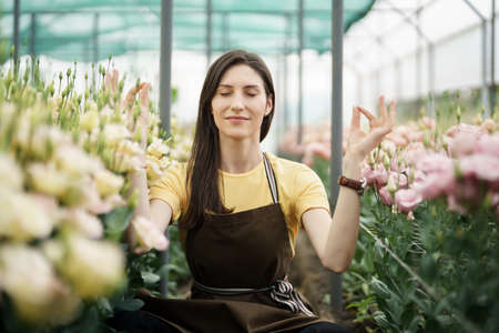 Pretty women relaxing among flowers while sitting in a meditation pose in the green houseの写真素材