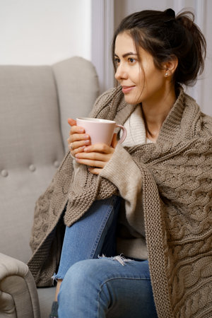 Smiling lady in smart trendy wear is sitting on armchair with a cup of tea. Smiling, sitting in relaxing atmosphere indoors at home, nice design.の写真素材