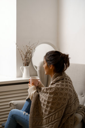 Smiling lady in smart trendy wear is sitting on armchair with a cup of tea. Smiling, sitting in relaxing atmosphere indoors at home, nice design.の写真素材