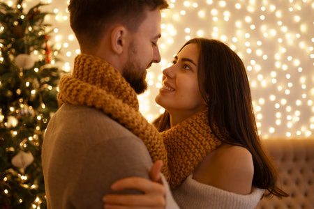Two cheerful lovely sweet tender beautiful adorable cute romantic married spouses husband and wife enfolding in one snood fot two near fir tree in houseの写真素材