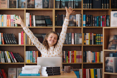Attractive happy young girl student studying at the college library, sitting at the desk, using...