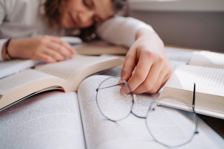 Young women got asleep on the books while studying holding reading glasses