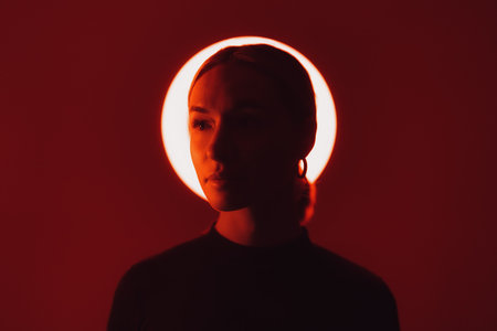 Woman in neon light against red backdropの写真素材