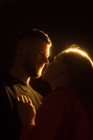 Romantic couple kissing in dark room against glowing orange lightの写真素材