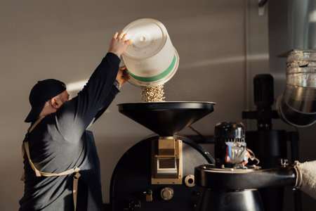Male worker pouring coffee beans into roasting machineの写真素材