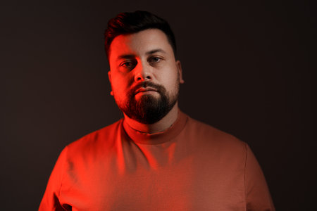 Thoughtful bearded man looking at camera on black background with neon illuminationの写真素材