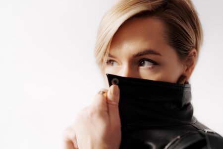 Woman with blond hair covering mouth with jacket collarの写真素材