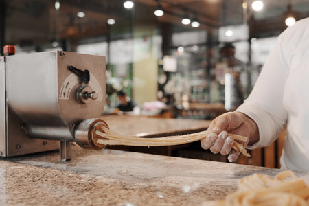 Crop cook preparing pasta with machine in restaurant kitchenの写真素材