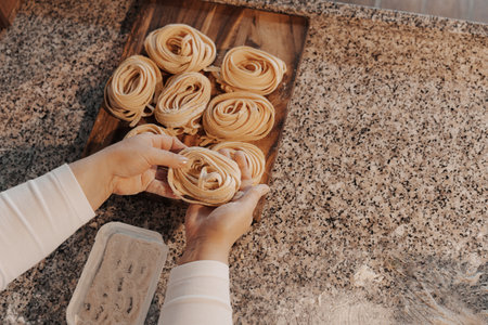 Crop housewife preparing homemade rolled tagliatelle pastaの写真素材