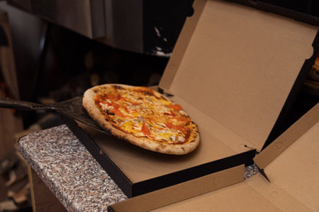 Anonymous male pizza chef putting hot pizza in box for deliveryの写真素材