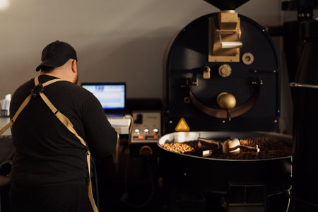 Man using laptop while working with coffee roasting machineの写真素材