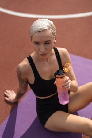 Fitness woman drinking water on yoga matの写真素材