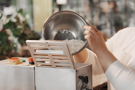 Crop female cook adding flour into pasta makerの写真素材