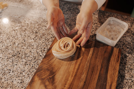 Crop housewife preparing homemade rolled tagliatelle pastaの写真素材