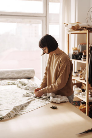 Creative woman focused on sewing fabric in sunlit workshop