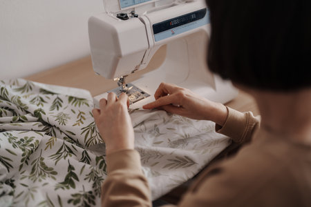 Craftswoman sewing fabric with machine in workshop