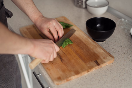 Person chopping fresh green vegetables in kitchenの写真素材